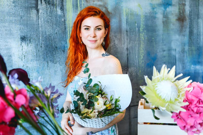 L'employé de magasin féminin de cheveux rouges gais avec du charme se tient prêt la boîte en bois avec des fleurs avec le pourpre