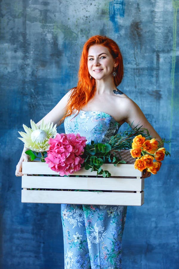 L'employé de magasin féminin de cheveux rouges gais avec du charme tient la boîte en bois avec des fleurs avec le pourpre d'horte