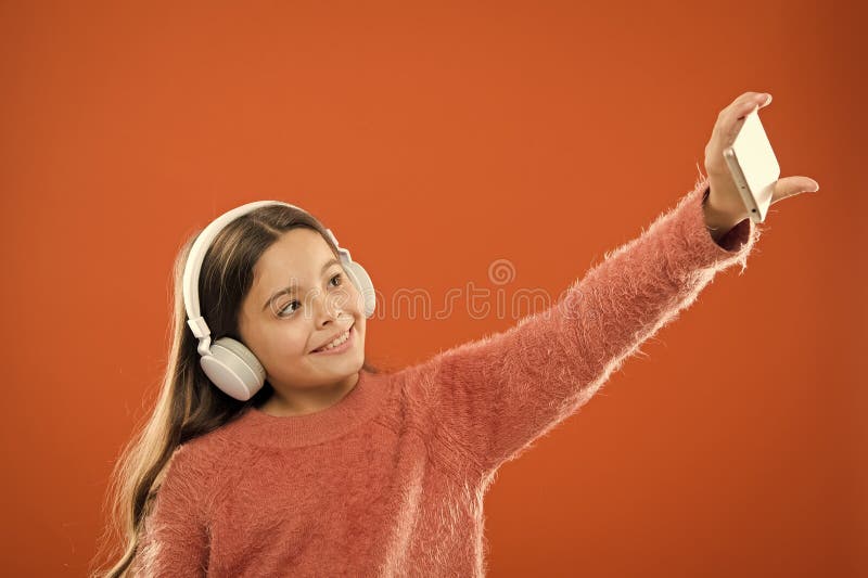 L'enfant de fille ?coutent les ?couteurs modernes et le smartphone de musique prenant le selfie Obtenez l'abonnement de musique A photo libre de droits L'enfant de fille ?coutent les ?couteurs modernes et le smartphone de musique prenant le selfie Obtenez l'abonnement de musique A photo libre de droits