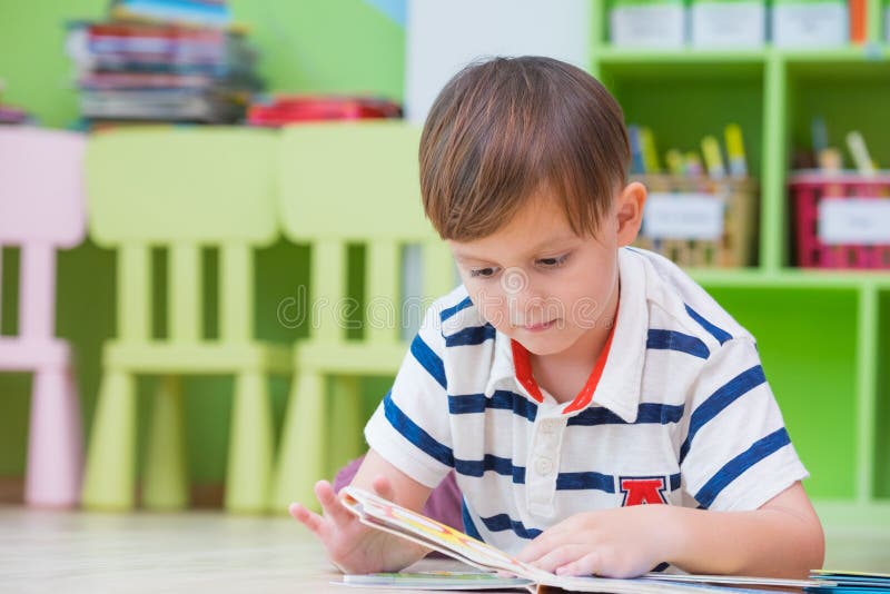 L'enfant de garçon fixent sur le livre de conte de plancher et de lecture dans la bibliothèque préscolaire, concept d'éducation d photographie stock L'enfant de garçon fixent sur le livre de conte de plancher et de lecture dans la bibliothèque préscolaire, concept d'éducation d photographie stock