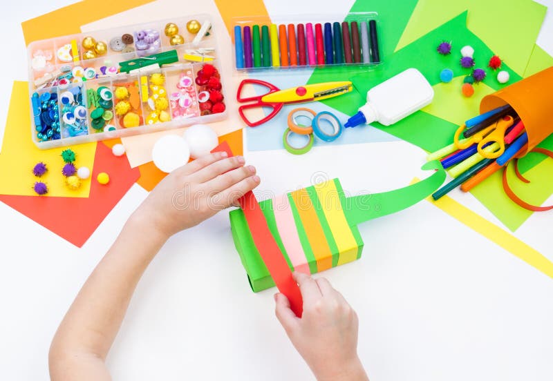 Child makes a hack box chameleon. Material for creativity on a white background. Baby hand. Rainbow colored paper. Child makes a hack box chameleon. Material for creativity on a white background. Baby hand. Rainbow colored paper