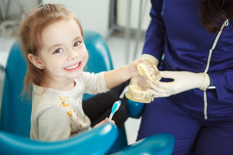 L'enfant gai s'assied dans la chaise de dentiste et se renseigne sur le toothcare photo libre de droits L'enfant gai s'assied dans la chaise de dentiste et se renseigne sur le toothcare photo libre de droits