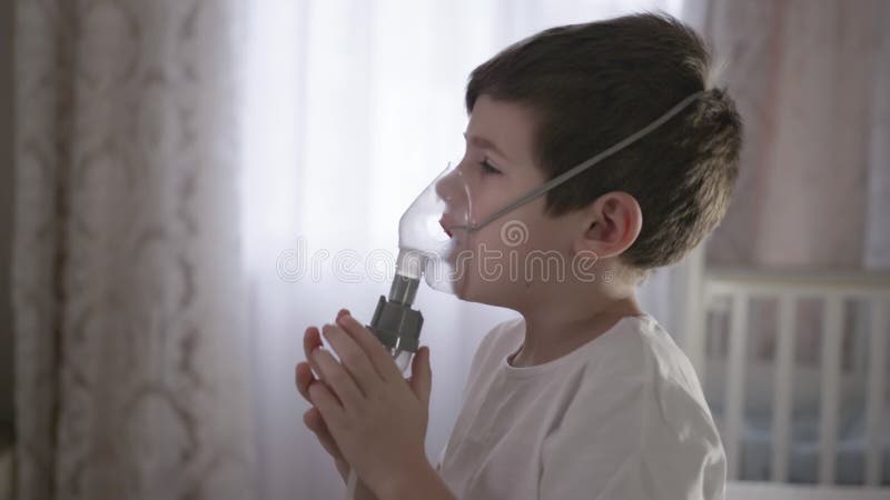 Petit garçon dans un masque, les traitements des voies respiratoires avec  un pulvérisateur à la maison. Siège bébé avec un nébulisateur dans sa  bouche, inhalateur, le traitement de la bronchite Photo Stock 