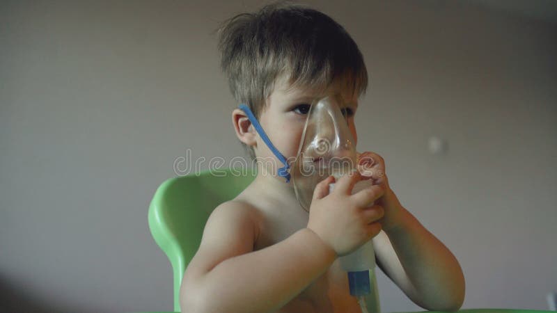 Petit garçon dans un masque, les traitements des voies respiratoires avec  un pulvérisateur à la maison. Siège bébé avec un nébulisateur dans sa  bouche, inhalateur, le traitement de la bronchite Photo Stock 