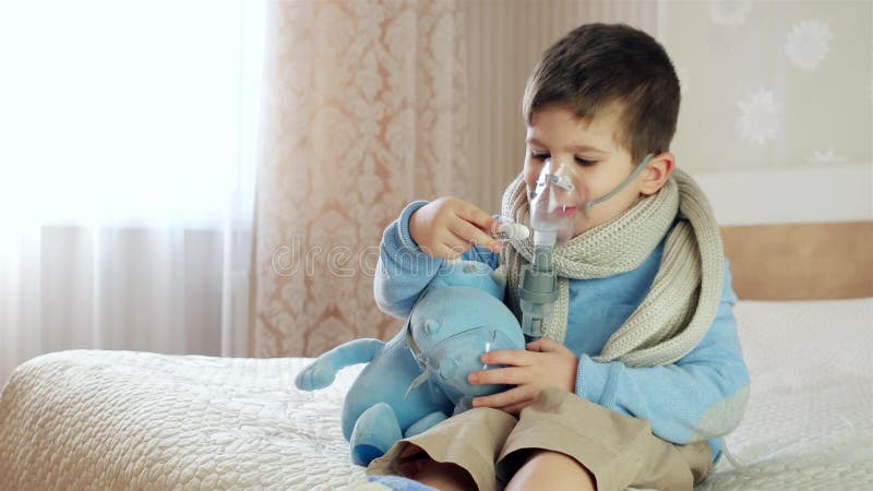 Petit garçon dans un masque, les traitements des voies respiratoires avec  un pulvérisateur à la maison. Siège bébé avec un nébulisateur dans sa  bouche, inhalateur, le traitement de la bronchite Photo Stock 