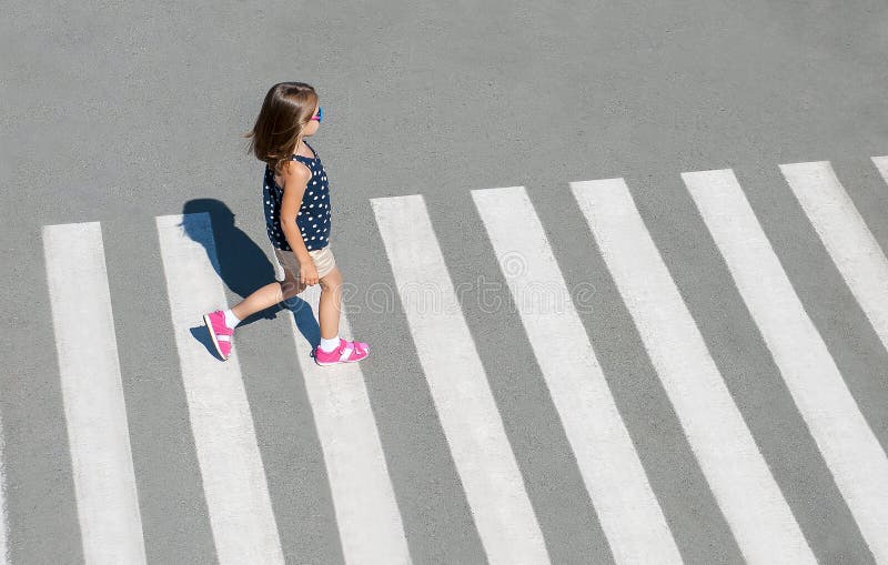 Stylish child in fashion clothes is walking along summer city crosswalk. Kid on pedestrian side walk. Concept pedestrians passing a crosswalk. Traffic rules. From top view. Shadow at zebra crossing. Stylish child in fashion clothes is walking along summer city crosswalk. Kid on pedestrian side walk. Concept pedestrians passing a crosswalk. Traffic rules. From top view. Shadow at zebra crossing