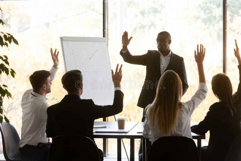 Group meeting led by African coach or company boss and corporate staff take part in voting raising hands express opinion unanimously. Concept of teamwork, unity, common decision and like-minded people. Group meeting led by African coach or company boss and corporate staff take part in voting raising hands express opinion unanimously. Concept of teamwork, unity, common decision and like-minded people