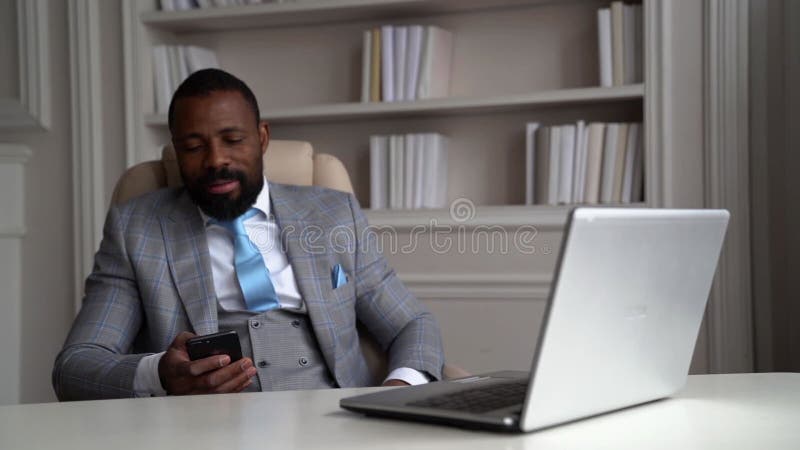 L'entrepreneur afro-américain détendu repose dans son bureau et nouvelles de visualisation dans les filets sociaux dans le smartph banque de vidéos