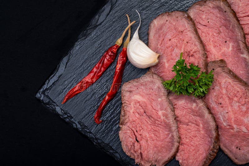 L'erba affettata Fed Corn Roast Beef ha guarnito con aglio, prezzemolo riccio fresco ed il Cile rosso secco De Arbol Peppers immagine stock L'erba affettata Fed Corn Roast Beef ha guarnito con aglio, prezzemolo riccio fresco ed il Cile rosso secco De Arbol Peppers immagine stock