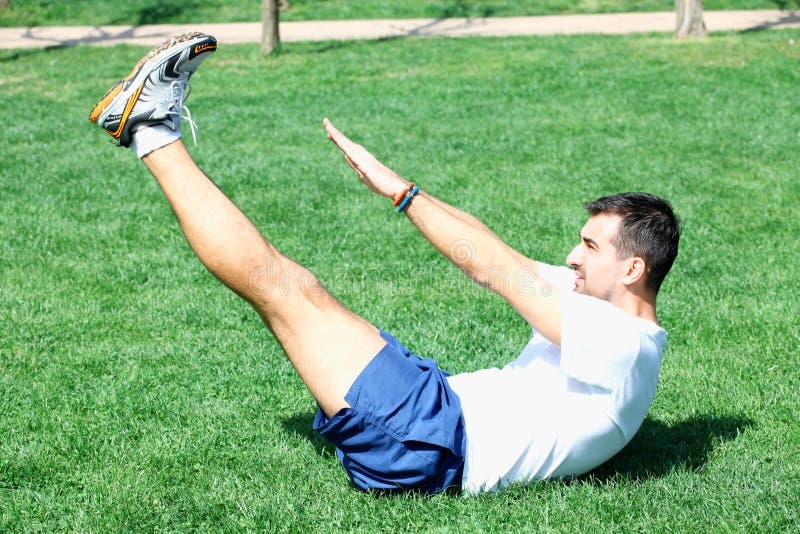 L'esercitazione dell'uomo di forma fisica si siede su fuori in erba di estate MA adatto fotografia stock L'esercitazione dell'uomo di forma fisica si siede su fuori in erba di estate MA adatto fotografia stock