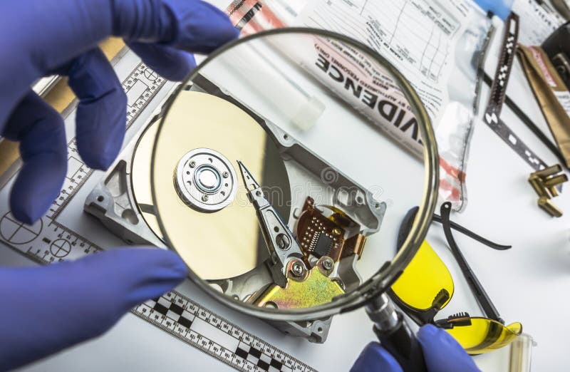 L'esperto nella polizia esamina con il disco rigido della lente d'ingrandimento alla ricerca di prova immagine stock L'esperto nella polizia esamina con il disco rigido della lente d'ingrandimento alla ricerca di prova immagine stock