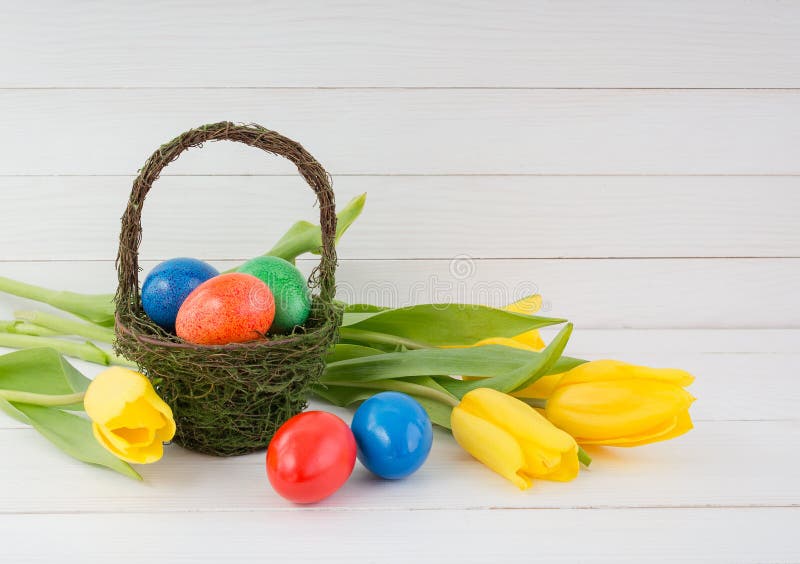 L'estere eggs la merce nel carrello ed i tulipani gialli su fondo di legno bianco immagine stock L'estere eggs la merce nel carrello ed i tulipani gialli su fondo di legno bianco immagine stock