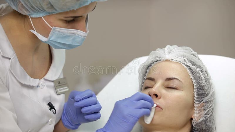 L'estetista pulisce il fronte del paziente femminile con la spugna del cotone prima della procedura disinfezione