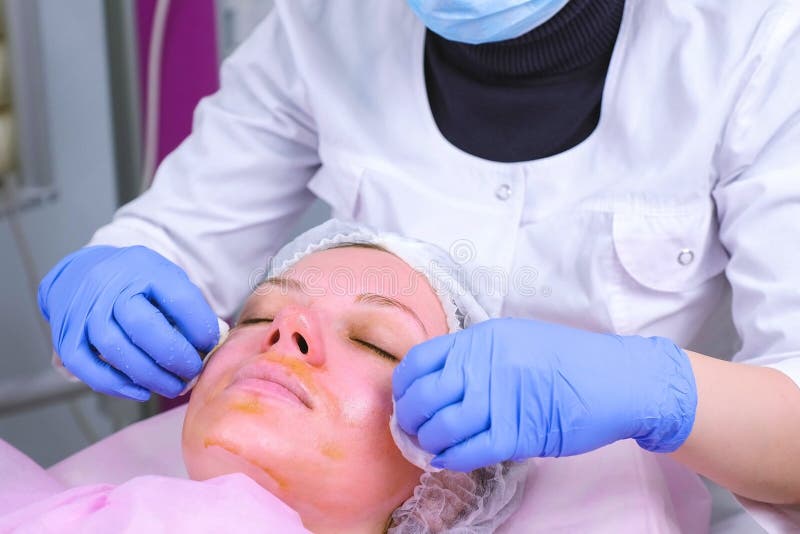 L'esth?ticien lave l'?pluchage chimique de protections de coton du visage du patient Nettoyage de la peau de visage et ?clairage image stock L'esth?ticien lave l'?pluchage chimique de protections de coton du visage du patient Nettoyage de la peau de visage et ?clairage image stock