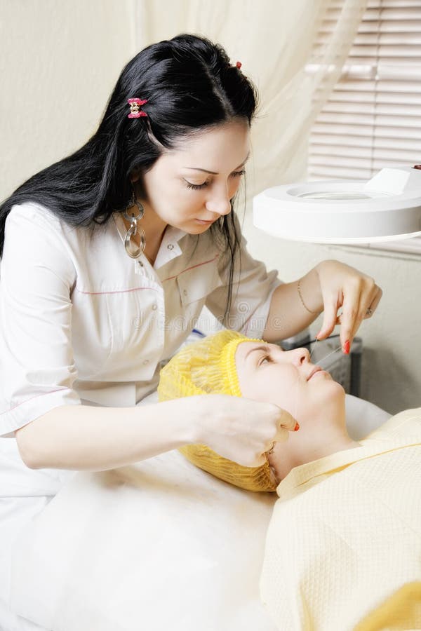 Brunette beautician makes threading hair removal procedure to middle-aged caucasian women laying down in chair. Brunette beautician makes threading hair removal procedure to middle-aged caucasian women laying down in chair