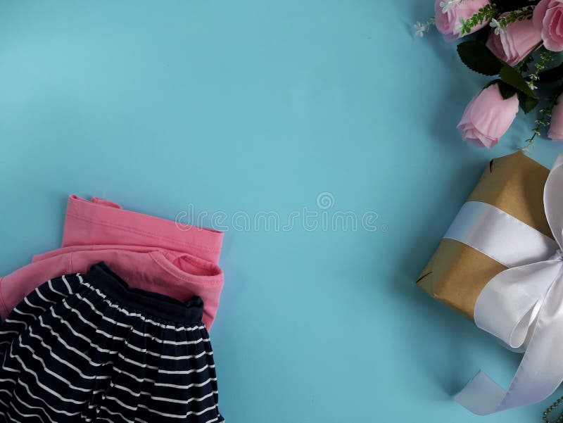 L'habillement lumineux de couleur, s'est levé T-shirt, jupe de toile de marine, le boîte-cadeau, fleurs sur le fond bleu image stock L'habillement lumineux de couleur, s'est levé T-shirt, jupe de toile de marine, le boîte-cadeau, fleurs sur le fond bleu image stock