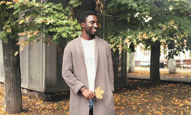 L'homme africain de sourire heureux de portrait de mode regardant loin tient les feuilles jaunes d'érable en automne photo stock L'homme africain de sourire heureux de portrait de mode regardant loin tient les feuilles jaunes d'érable en automne photo stock