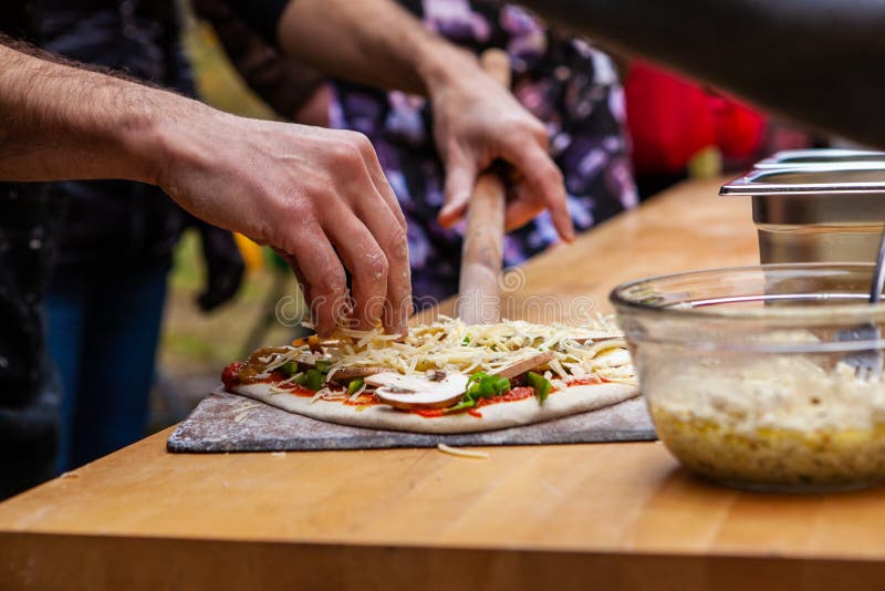 L'homme ajoute des habillages sur sa pâte fraîchement malaxée de pizza photos stock L'homme ajoute des habillages sur sa pâte fraîchement malaxée de pizza photos stock