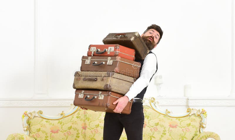 L'homme avec la barbe et la moustache portant le costume classique livre le bagage, fond intérieur blanc de luxe Butler et servic photo stock L'homme avec la barbe et la moustache portant le costume classique livre le bagage, fond intérieur blanc de luxe Butler et servic photo stock