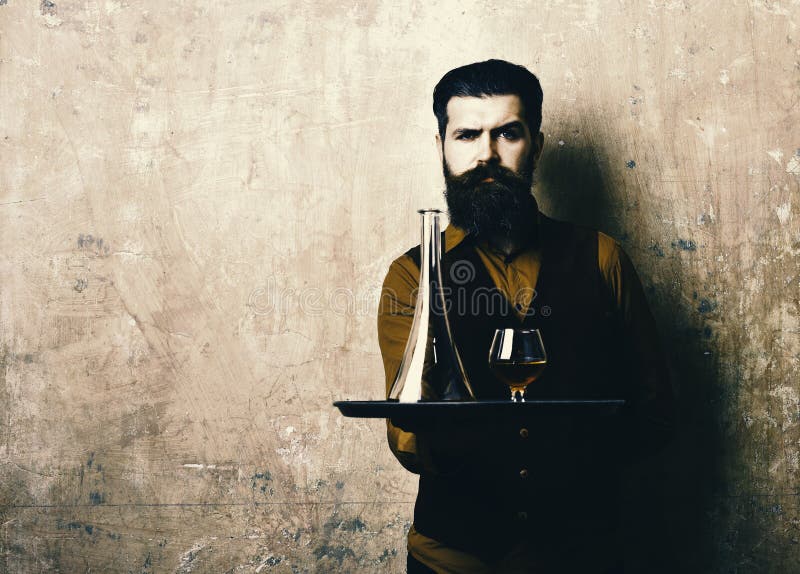 L'homme avec la barbe tient le cognac sur le fond beige, l'espace de copie Service et concept de boissons de restaurant Serveur a images libres de droits L'homme avec la barbe tient le cognac sur le fond beige, l'espace de copie Service et concept de boissons de restaurant Serveur a images libres de droits