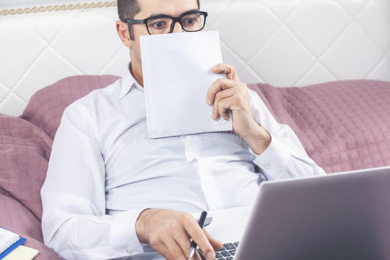 Un Homme Est Assis Dans Son Lit Avec Un Ordinateur Portable Devant Une Guirlande  Lumineuse.