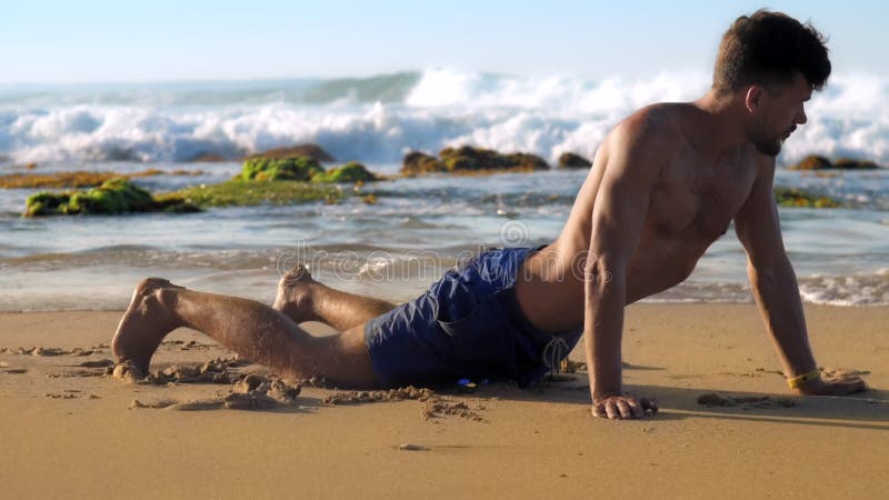 L'homme barbu bel se tient sur la plage sablonneuse en position de yoga