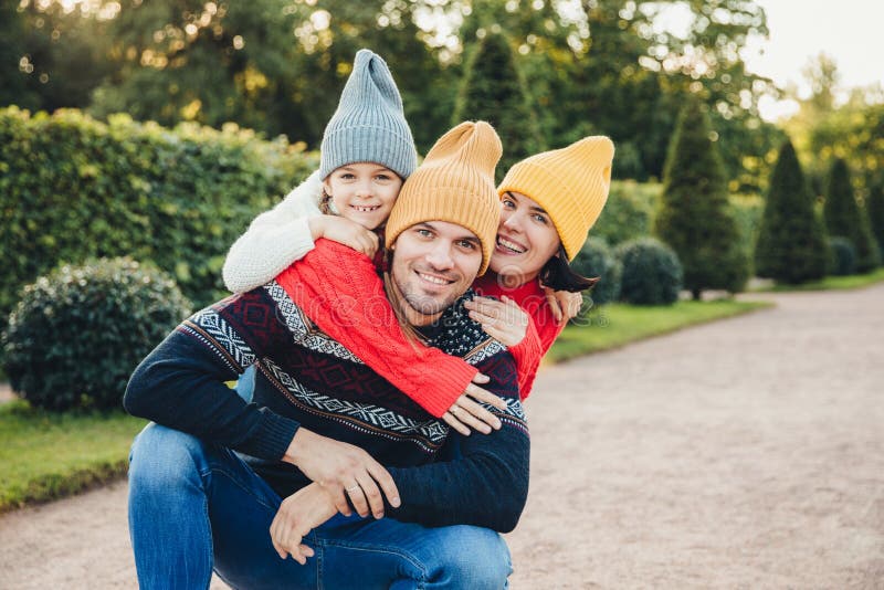L'homme bel a de bonnes relations avec l'épouse et la petite fille qui l'embrassent du dos, ont des sourires agréables Jeunes ami photographie stock L'homme bel a de bonnes relations avec l'épouse et la petite fille qui l'embrassent du dos, ont des sourires agréables Jeunes ami photographie stock