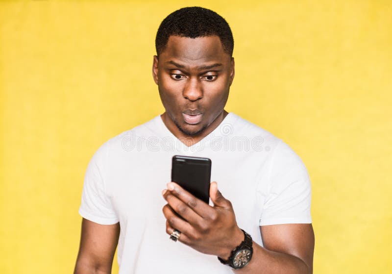 L'homme bel embarrassé et inquiété d'Afro-américain tient le smartphone, regarde fixement avec l'expression étonnée images stock L'homme bel embarrassé et inquiété d'Afro-américain tient le smartphone, regarde fixement avec l'expression étonnée images stock