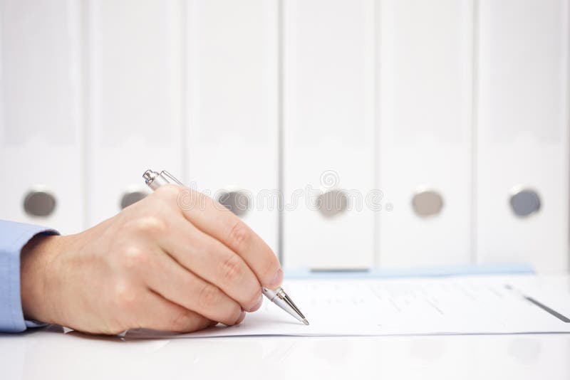 Businessman or accountant is signing document with binders in background. Businessman or accountant is signing document with binders in background