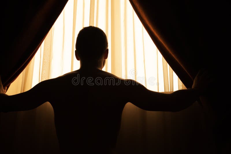 L'homme dans la chambre noire ouvre des rideaux sur la fenêtre photos stock L'homme dans la chambre noire ouvre des rideaux sur la fenêtre photos stock