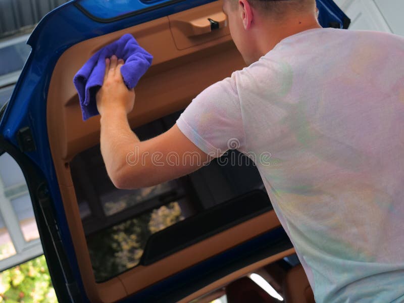 L'homme dans la voiture sèche de l'intérieur de toutes les parties de la voiture en utilisant un chiffon et un pistolet à air c photographie stock libre de droits