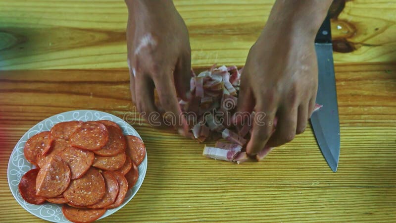 L'homme de gros plan de vue de dessus à la main sépare de petits morceaux de jambon tranché sur la table en bois banque de vidéos