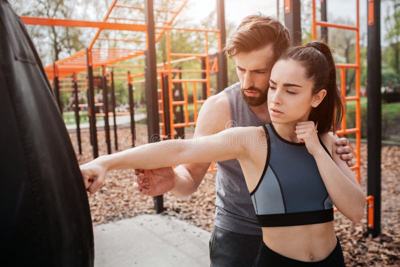 L'homme et la femme sportifs se tiennent en parc et s'exercent ensemble La fille essaye à la boxe tandis que son entraîneur est image libre de droits L'homme et la femme sportifs se tiennent en parc et s'exercent ensemble La fille essaye à la boxe tandis que son entraîneur est image libre de droits