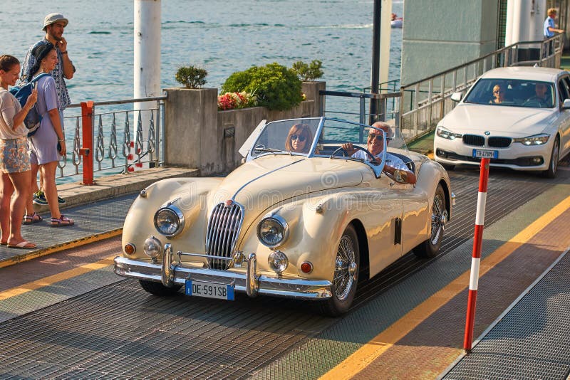 L'homme heureux chasse son vintage Jaguar beige XK120, une voiture de sport construite par Jaguar vers 1950, du ferry-boat photo libre de droits L'homme heureux chasse son vintage Jaguar beige XK120, une voiture de sport construite par Jaguar vers 1950, du ferry-boat photo libre de droits