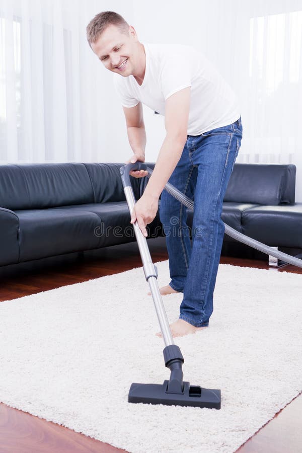 L'homme heureux nettoie dans la salle moderne avec le vide. photo stock L'homme heureux nettoie dans la salle moderne avec le vide. photo stock