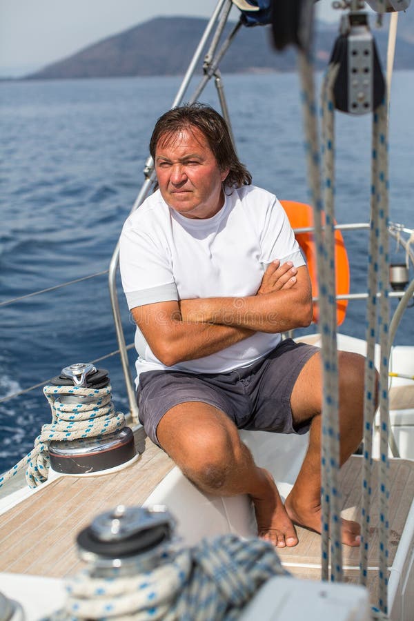 L'homme mûr s'assied sur son yacht de voile photo stock L'homme mûr s'assied sur son yacht de voile photo stock