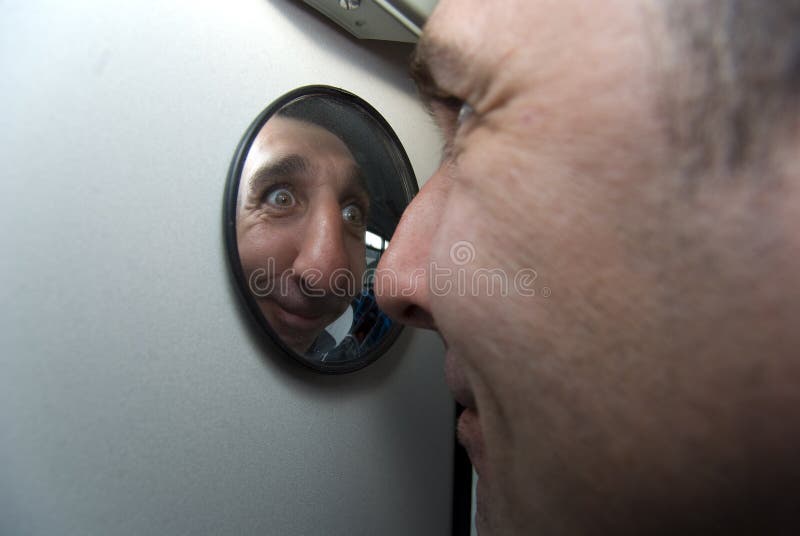 L'homme maladroit regarde dans le miroir rond photographie stock L'homme maladroit regarde dans le miroir rond photographie stock