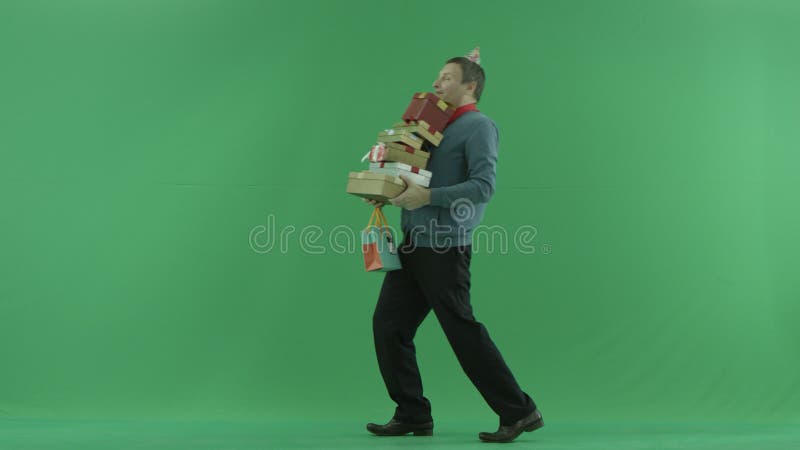 L'homme mûr marche avec la pile des cadeaux d'anniversaire, fond vert de clé de chroma