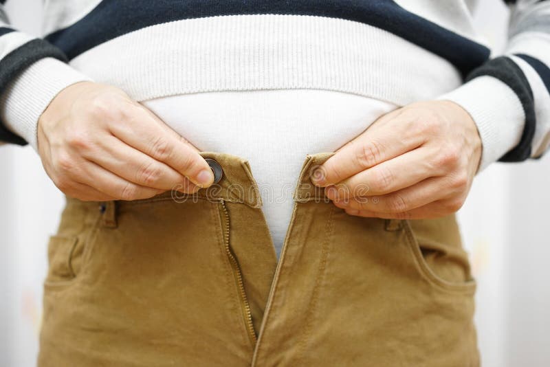 Man is unable to close his pants because of gaining weight . Man is unable to close his pants because of gaining weight .