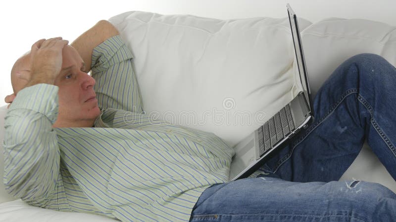 L'homme s'asseyant sur Sofa Doing Business Using Laptop font des gestes déçus photographie stock L'homme s'asseyant sur Sofa Doing Business Using Laptop font des gestes déçus photographie stock