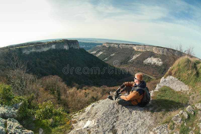 L'homme s'assied au bord d'une falaise sur le plateau de Mangup photo stock L'homme s'assied au bord d'une falaise sur le plateau de Mangup photo stock