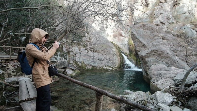 L'homme se tient sur le pont en bois au-dessus de la rivière dans la forêt, prenant des photos clips vidéos