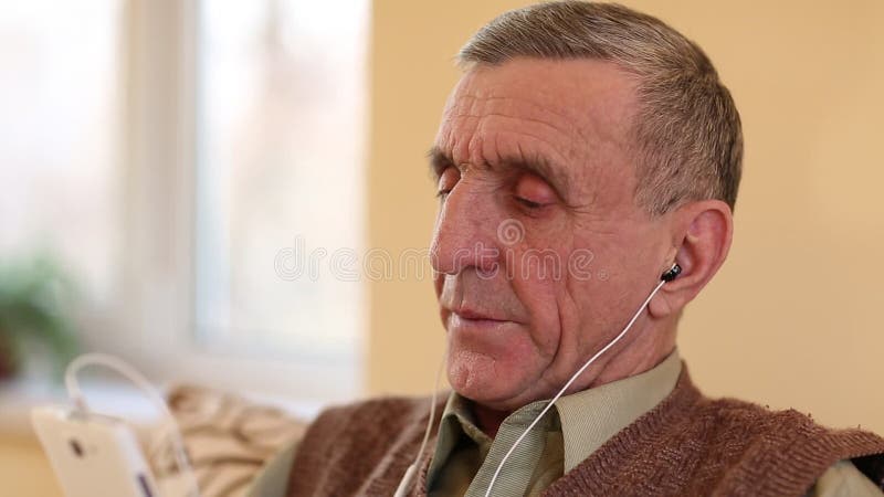 L'homme supérieur avec le smartphone blanc s'assied sur le divan et écoute la musique