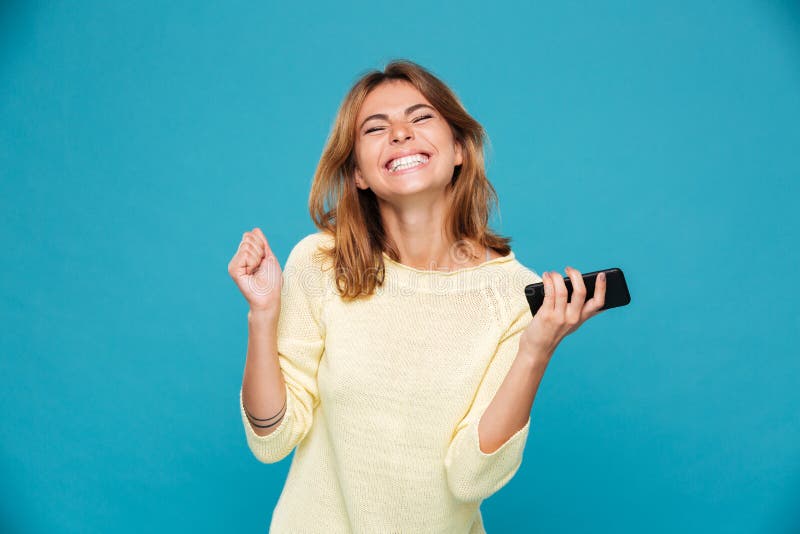 L'image de la femme heureuse dans le chandail tenant le smartphone et se réjouissent photo libre de droits