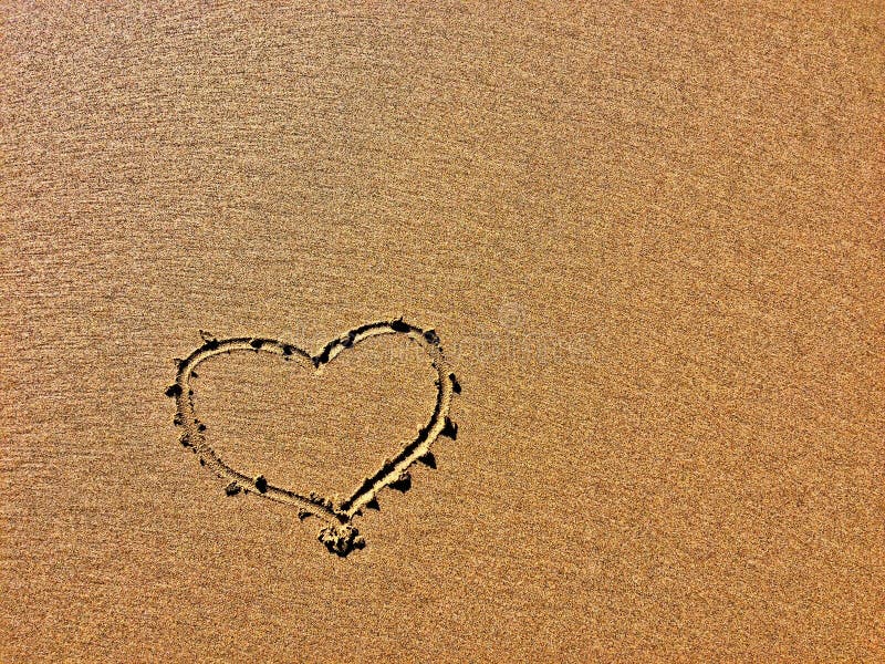 The image shows a heart shape drawn in the sand with fine grains. The image shows a heart shape drawn in the sand with fine grains.