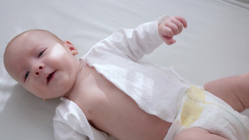 L'infante felice in pannolini si trova in letto bianco all'interno con luce naturale