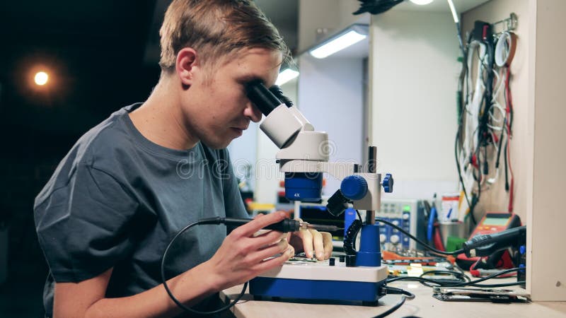 L'ingénieur mâle utilise un microscope pour garantir un microcircuit