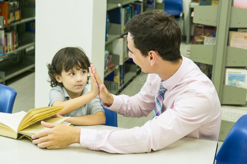 L'insegnante dell'uomo e lo studente del bambino imparano con il libro al backgro dello scaffale per libri fotografia stock libera da diritti L'insegnante dell'uomo e lo studente del bambino imparano con il libro al backgro dello scaffale per libri fotografia stock libera da diritti