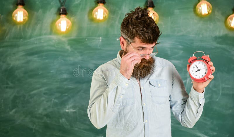 L'insegnante in occhiali tiene la sveglia Concetto di programma della scuola sveglia della tenuta dell'insegnante maschio, tempo fotografia stock libera da diritti L'insegnante in occhiali tiene la sveglia Concetto di programma della scuola sveglia della tenuta dell'insegnante maschio, tempo fotografia stock libera da diritti
