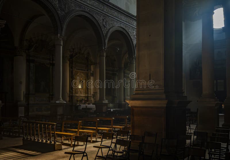 June 4, 2023 - Ferrara. The dark and silent interior of an ancient church, with light filtering through the rose window, illuminating the chairs and benches in the central nave. June 4, 2023 - Ferrara. The dark and silent interior of an ancient church, with light filtering through the rose window, illuminating the chairs and benches in the central nave